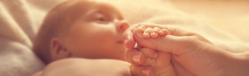 Maladie de Joubert : bébé allongé sur un lit tenant dans ses petits doigts une main d'un adulte.