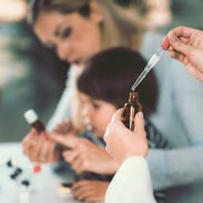 mère qui montre à son enfant un flacon d'homéopathie pendant qu'un médecin prélève du liquide avec une pipette