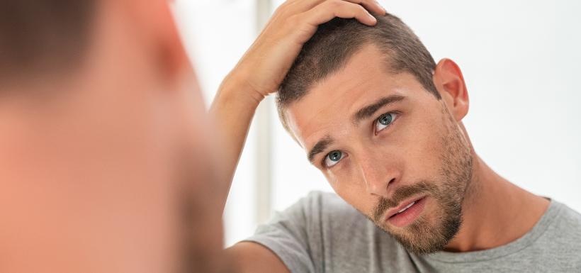 chute-cheveux-calvitie-fatalite-genetique-enjeu-sante Un homme qui se regarde dans le miroir en passant la main dans ses cheveux