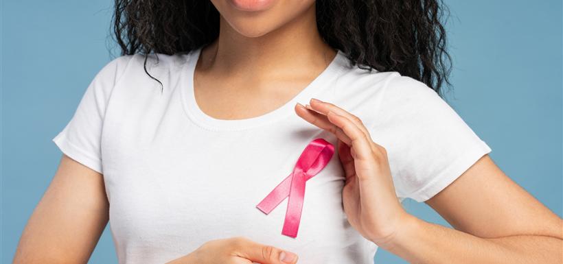 cancers-du-sein-differents-types-risques-traitements Une femme souriante, un ruban rose épinglé sur son t-shirt blanc, les mains en protection autour de sa poitrine