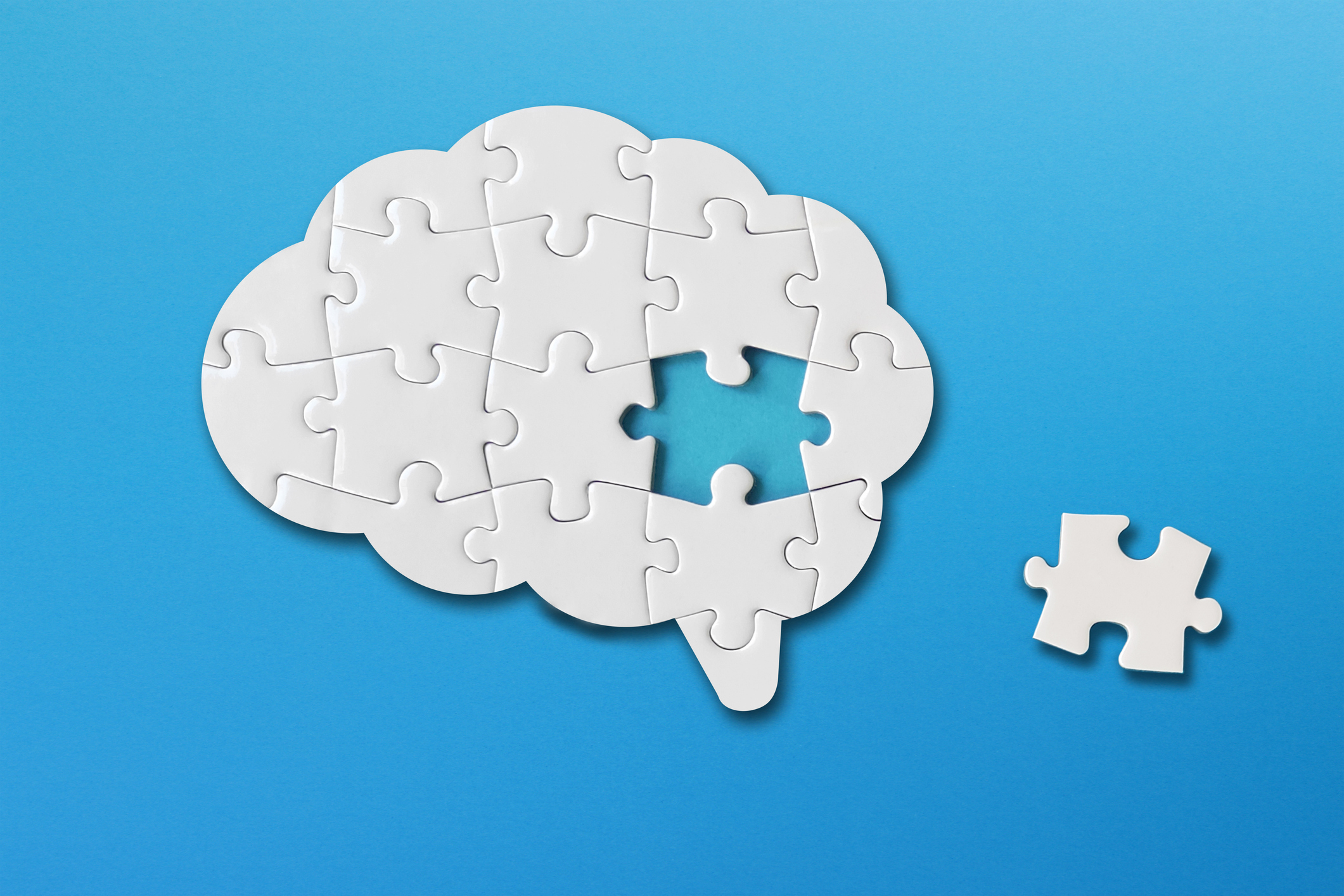 Brain shaped white jigsaw puzzle on blue background, a missing piece of the brain puzzle, mental health and problems with memory