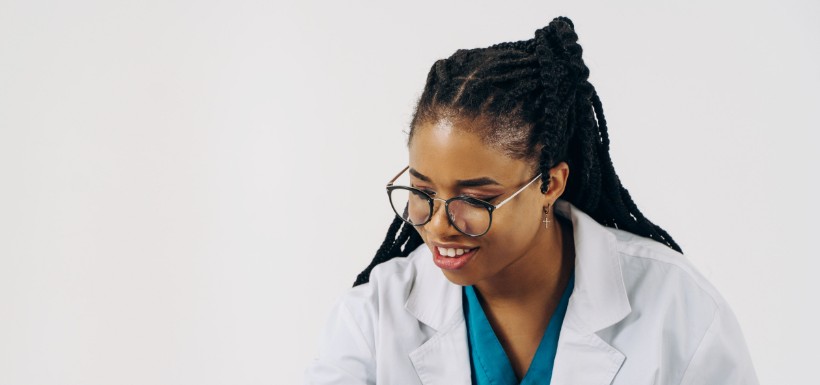 Une médecin souriante prend des notes sur un bloc, une tablette posée sur le bras